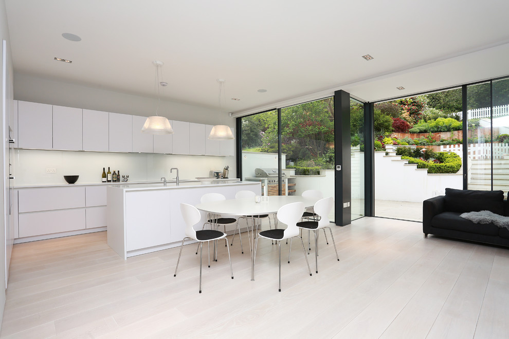 Inspiration for a contemporary open plan kitchen in London with flat-panel cabinets, white cabinets, composite countertops, an island and light hardwood flooring.
