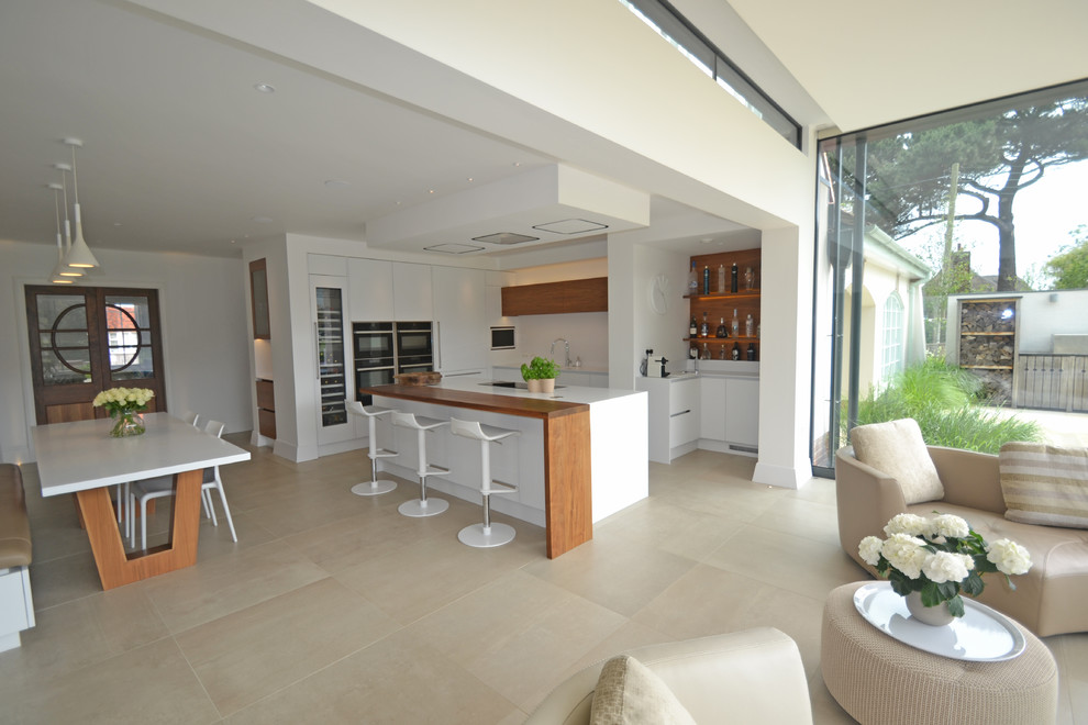 Modern inredning av ett stort kök, med släta luckor, vita skåp, vitt stänkskydd, rostfria vitvaror, klinkergolv i porslin och en köksö