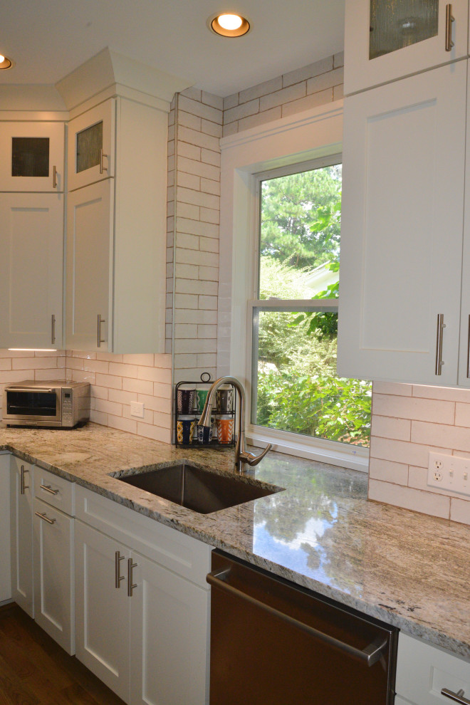 Exempel på ett stort klassiskt beige beige kök, med en dubbel diskho, luckor med infälld panel, vita skåp, granitbänkskiva, vitt stänkskydd, stänkskydd i keramik, rostfria vitvaror, ljust trägolv, en köksö och brunt golv