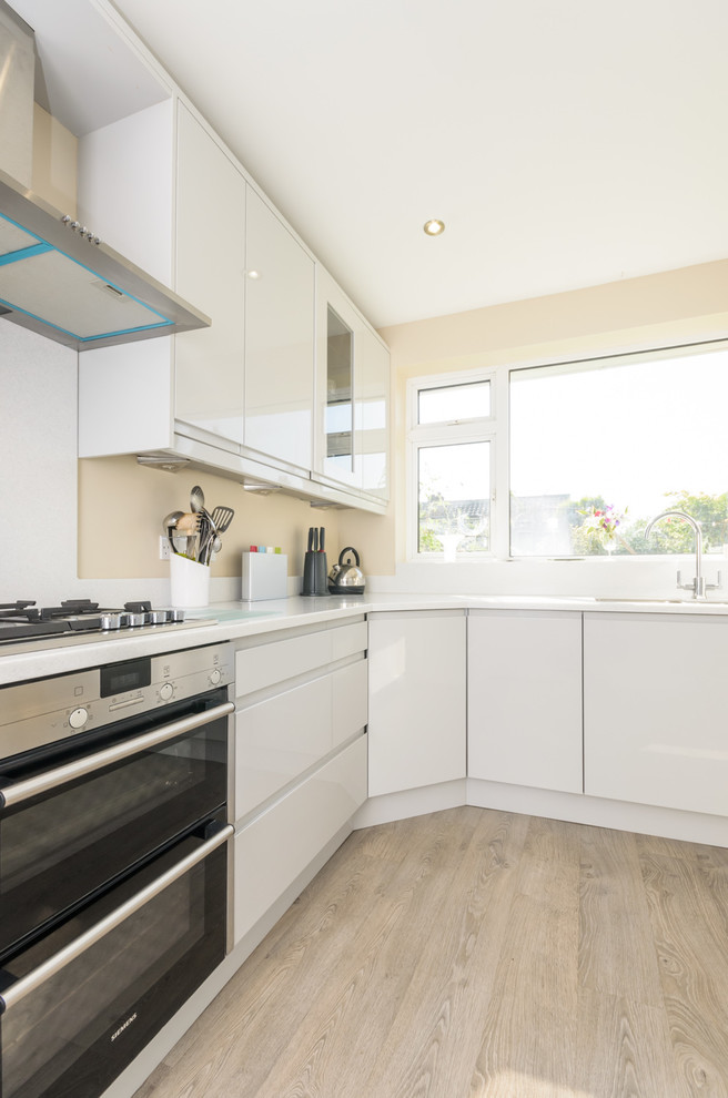 Foto di una cucina minimalista di medie dimensioni con ante bianche, top in superficie solida, paraspruzzi bianco e elettrodomestici da incasso