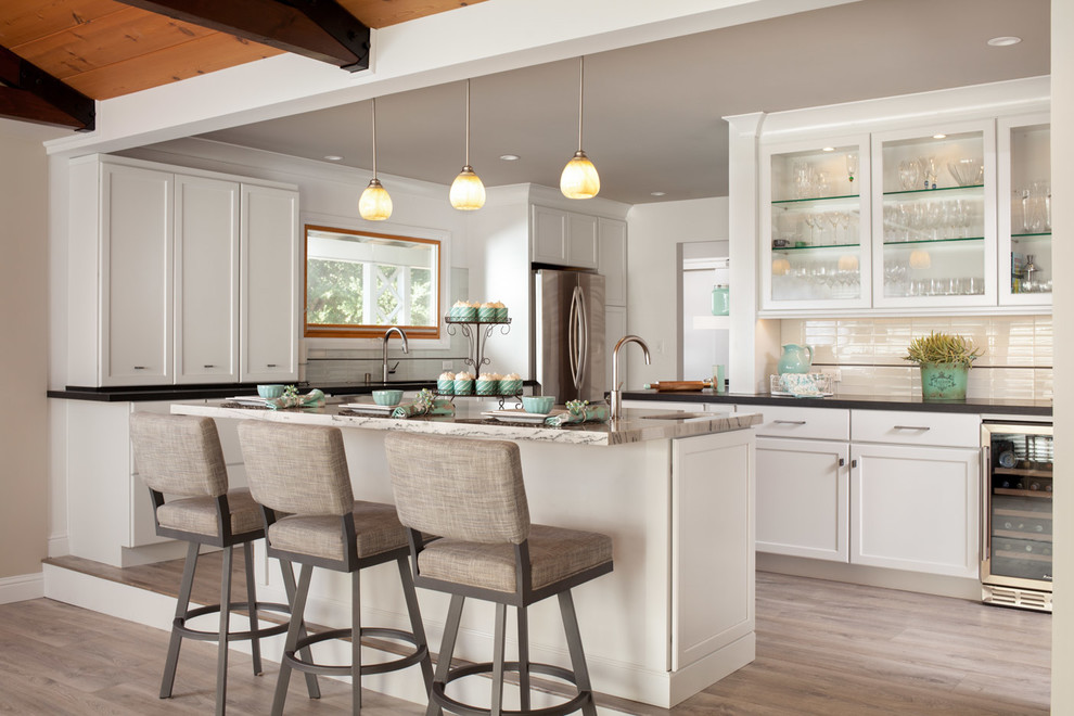 This is an example of a classic kitchen in San Francisco with recessed-panel cabinets, white cabinets, stainless steel appliances, light hardwood flooring, an island and black worktops.