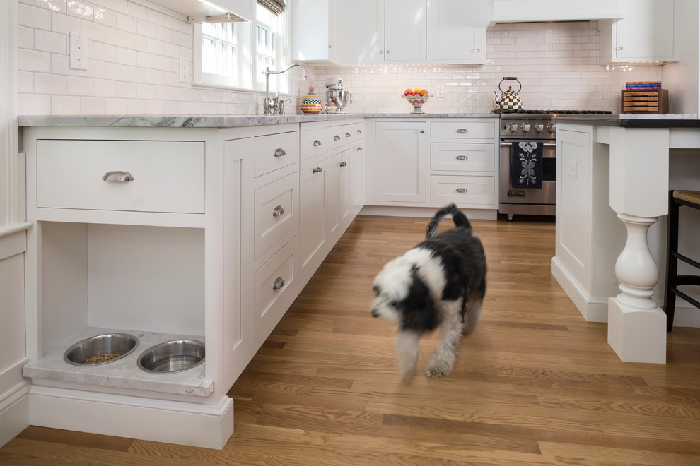 Inspiration for a large timeless l-shaped medium tone wood floor eat-in kitchen remodel in Boston with a single-bowl sink, white cabinets, quartzite countertops, white backsplash, ceramic backsplash, stainless steel appliances and an island