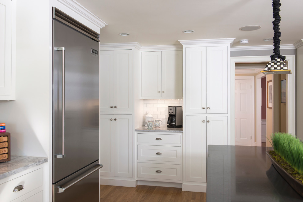 Example of a large classic l-shaped medium tone wood floor eat-in kitchen design in Boston with a single-bowl sink, white cabinets, quartz countertops, white backsplash, ceramic backsplash, stainless steel appliances and an island