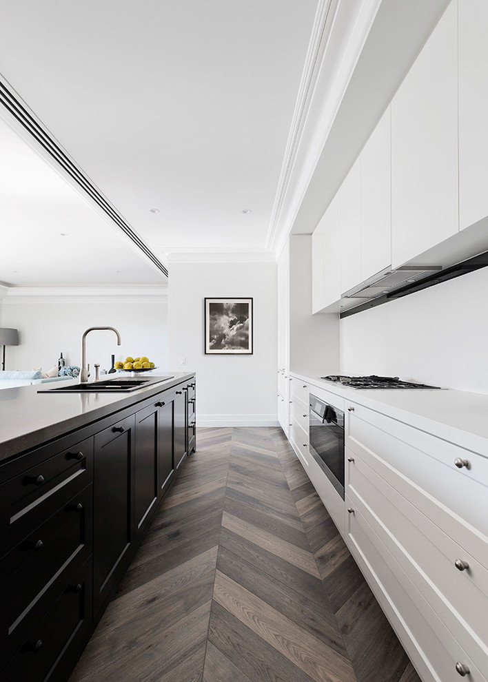 Inredning av ett minimalistiskt kök, med en nedsänkt diskho, skåp i shakerstil, rostfria vitvaror, mellanmörkt trägolv, en köksö och brunt golv