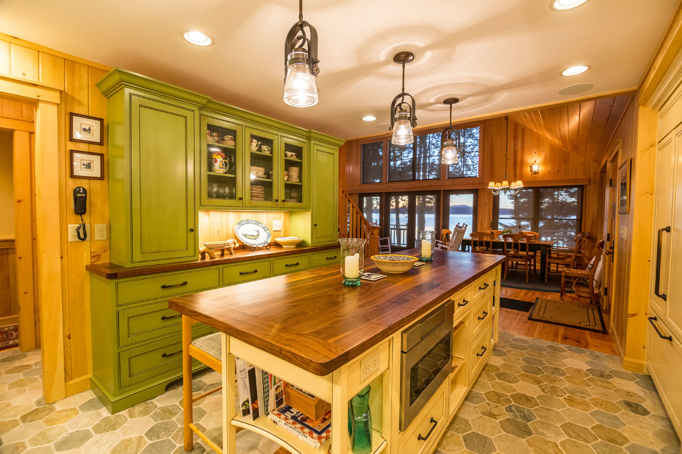 Rustik inredning av ett mellanstort kök, med luckor med profilerade fronter, skåp i slitet trä, träbänkskiva, beige stänkskydd, stänkskydd i travertin, integrerade vitvaror, skiffergolv, en köksö och flerfärgat golv