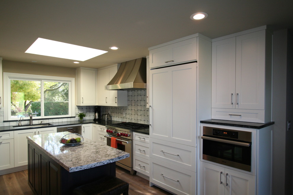 Inspiration for a large timeless u-shaped light wood floor open concept kitchen remodel in San Francisco with an undermount sink, recessed-panel cabinets, white cabinets, granite countertops, gray backsplash, ceramic backsplash, stainless steel appliances and a peninsula