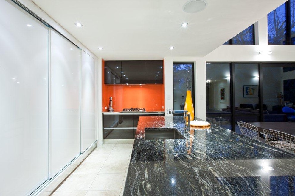 Diseño de cocina minimalista abierta con encimera de granito, fregadero bajoencimera, salpicadero naranja, salpicadero de vidrio templado y con blanco y negro