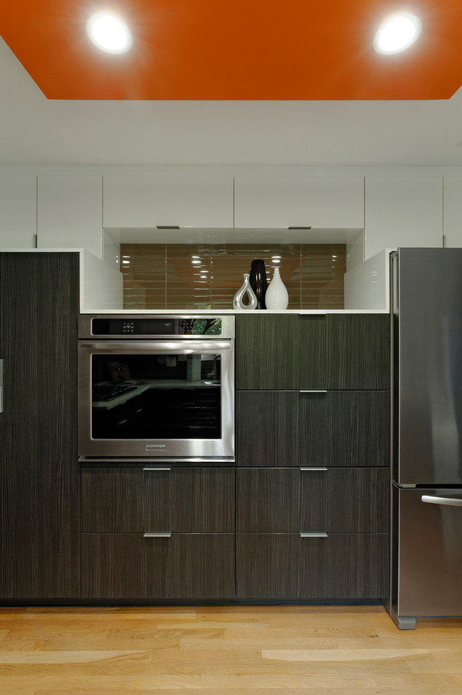Photo of a small contemporary u-shaped kitchen/diner in DC Metro with a submerged sink, flat-panel cabinets, dark wood cabinets, quartz worktops, beige splashback, glass tiled splashback, stainless steel appliances, light hardwood flooring and no island.