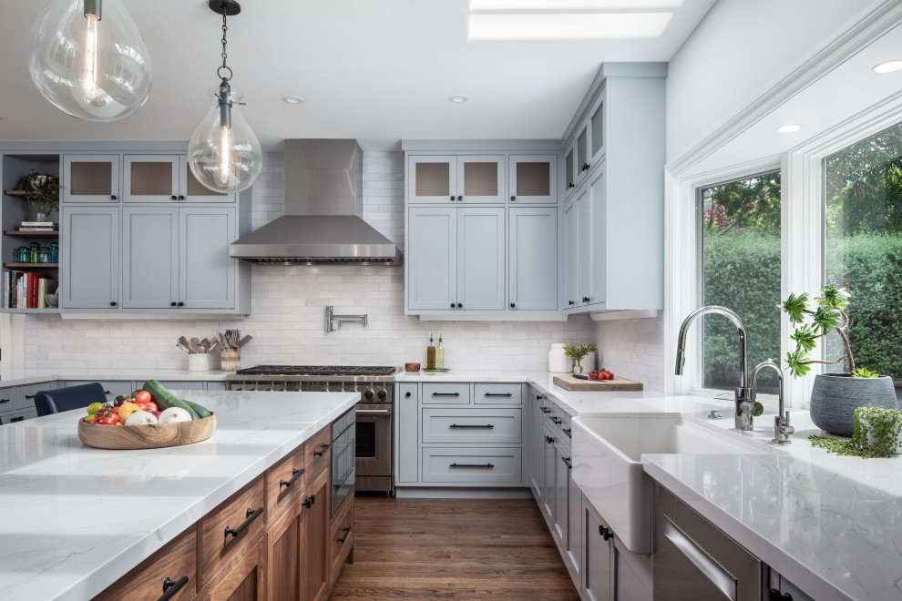 This is an example of a large traditional u-shaped open plan kitchen in Los Angeles with a belfast sink, engineered stone countertops, white splashback, porcelain splashback, stainless steel appliances, dark hardwood flooring, an island, brown floors, white worktops, shaker cabinets and grey cabinets.