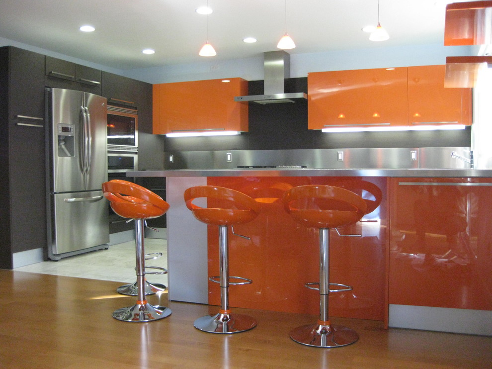 Foto på ett mellanstort funkis kök, med en dubbel diskho, släta luckor, orange skåp, bänkskiva i rostfritt stål, stänkskydd med metallisk yta, stänkskydd i metallkakel, rostfria vitvaror, mellanmörkt trägolv och en köksö