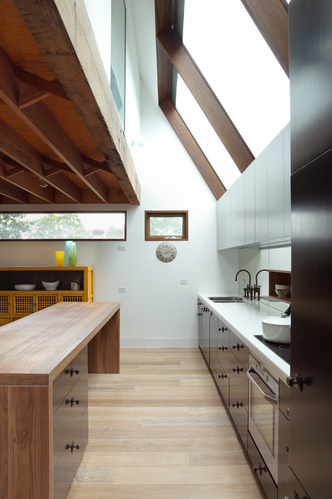 Zweizeilige, Mittelgroße Moderne Wohnküche mit Unterbauwaschbecken, schwarzen Schränken, Rückwand aus Spiegelfliesen, Kücheninsel und hellem Holzboden in Melbourne