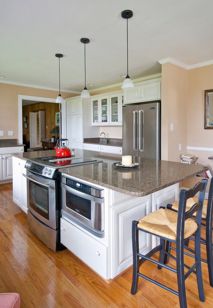 Klassisk inredning av ett mellanstort l-kök, med en dubbel diskho, luckor med upphöjd panel, vita skåp, granitbänkskiva, mellanmörkt trägolv, en köksö och brunt golv