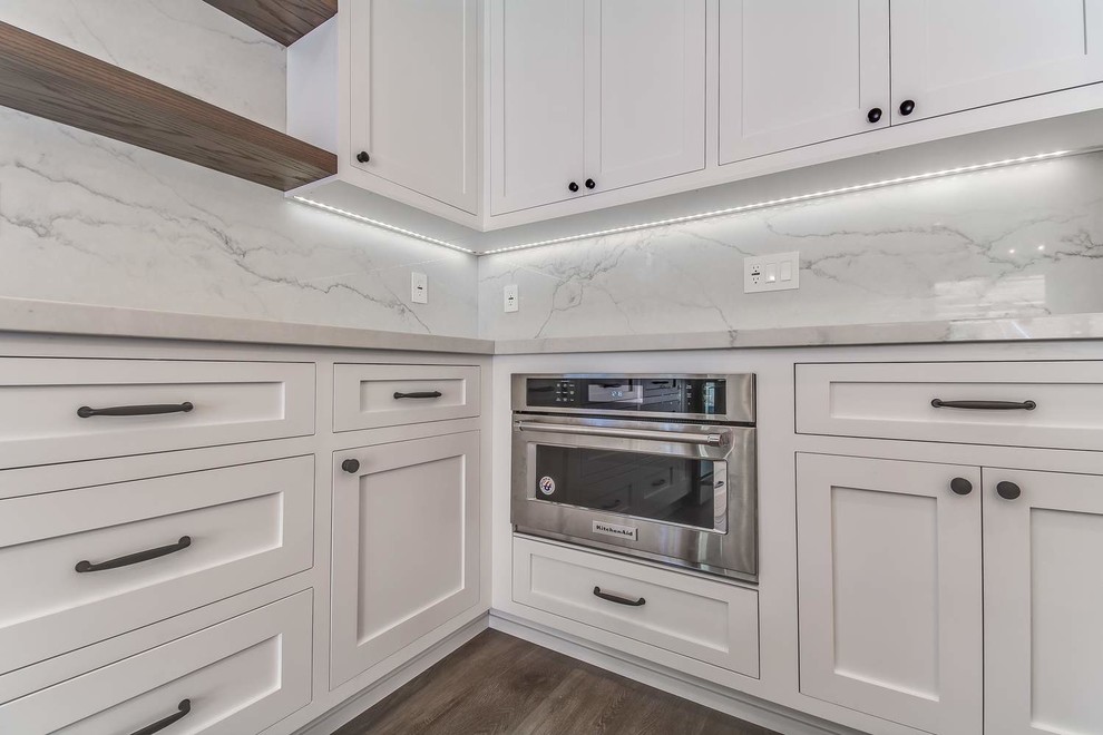 Mid-sized trendy u-shaped porcelain tile and brown floor eat-in kitchen photo in Orange County with an undermount sink, recessed-panel cabinets, white cabinets, quartz countertops, white backsplash, stone slab backsplash, stainless steel appliances, an island and white countertops