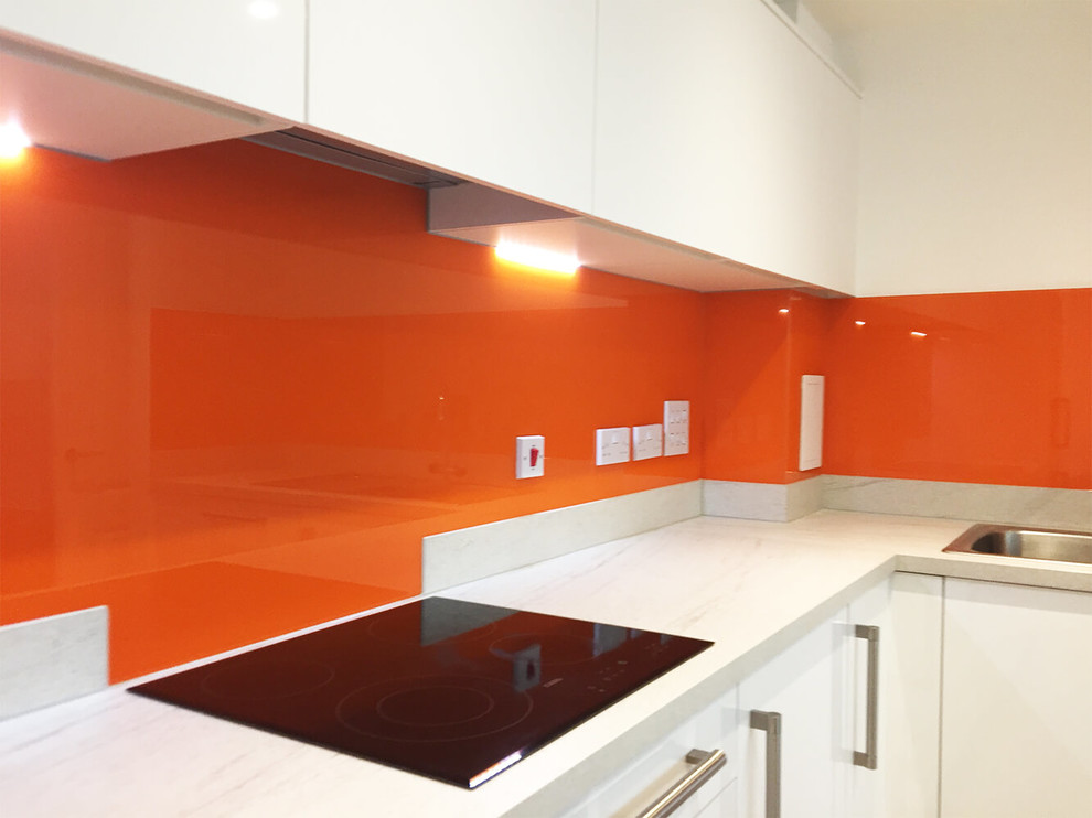 Bild på ett stort funkis kök och matrum, med släta luckor, vita skåp, marmorbänkskiva, orange stänkskydd och glaspanel som stänkskydd