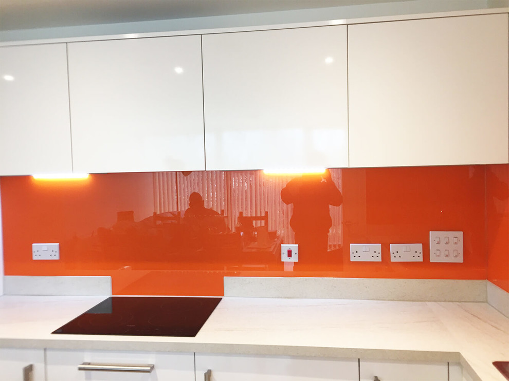 Große Moderne Wohnküche ohne Insel mit flächenbündigen Schrankfronten, weißen Schränken, Marmor-Arbeitsplatte, Küchenrückwand in Orange und Glasrückwand in Hertfordshire