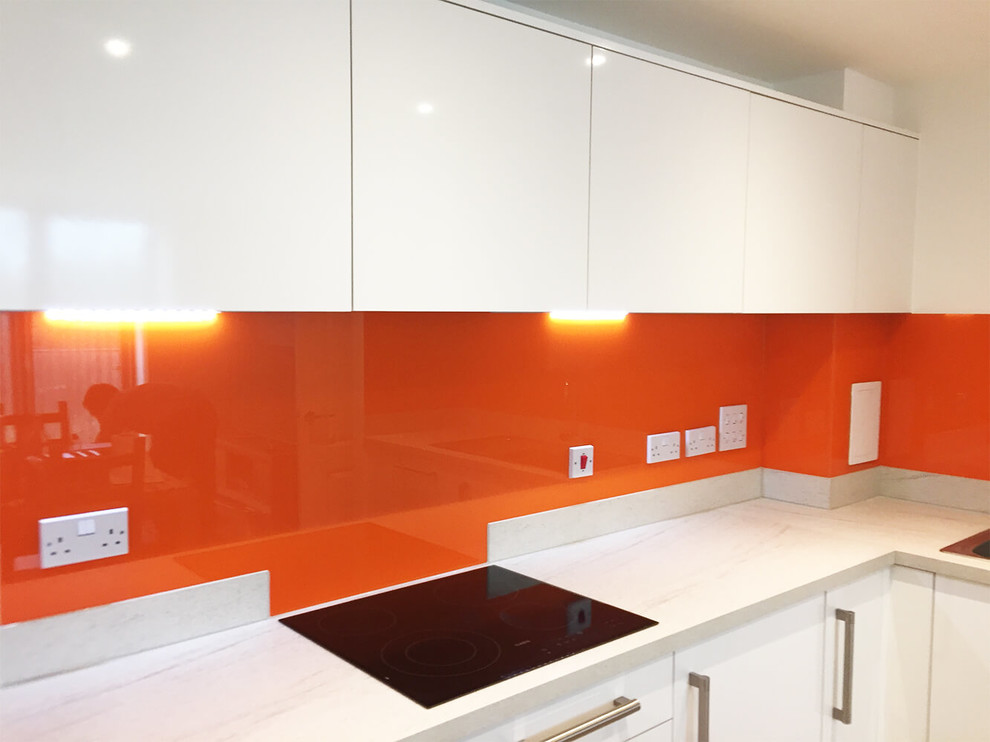 Cette image montre une grande cuisine américaine minimaliste avec un placard à porte plane, des portes de placard blanches, plan de travail en marbre, une crédence orange, une crédence en feuille de verre et aucun îlot.