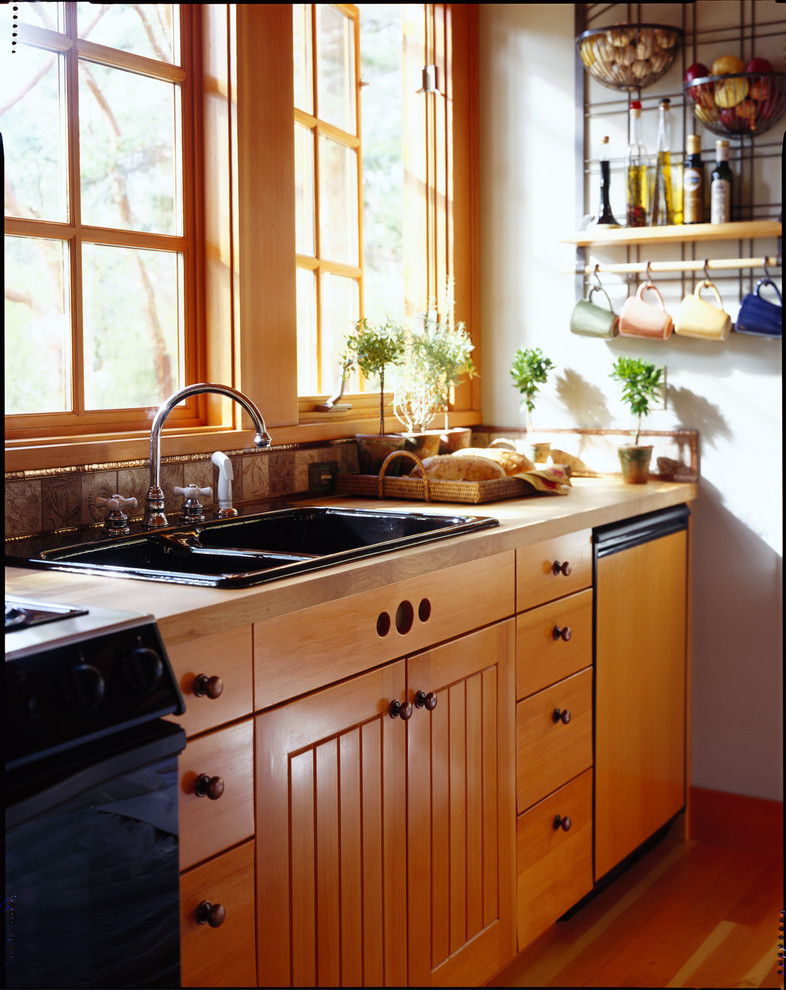 Example of a mountain style kitchen design in Seattle with a drop-in sink, flat-panel cabinets, medium tone wood cabinets, wood countertops and black appliances