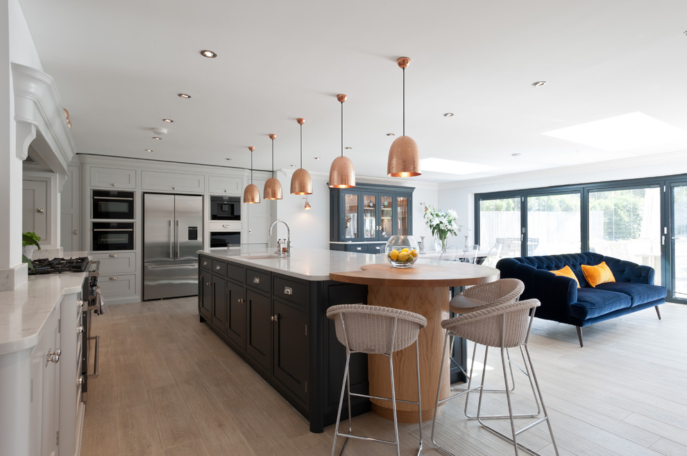Example of a large transitional l-shaped light wood floor and beige floor open concept kitchen design in Surrey with shaker cabinets, quartzite countertops, an island, white countertops, an undermount sink, white cabinets and black appliances