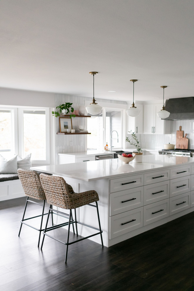 Inspiration for a large contemporary l-shaped laminate floor and brown floor open concept kitchen remodel in Portland with a farmhouse sink, shaker cabinets, white cabinets, quartzite countertops, white backsplash, marble backsplash, stainless steel appliances, an island and white countertops