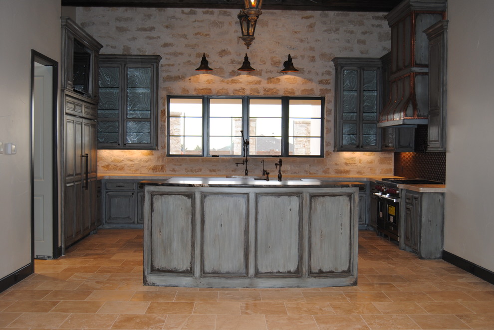 Inspiration for a mid-sized transitional u-shaped limestone floor enclosed kitchen remodel in Austin with an undermount sink, raised-panel cabinets, distressed cabinets, solid surface countertops, beige backsplash, paneled appliances and an island