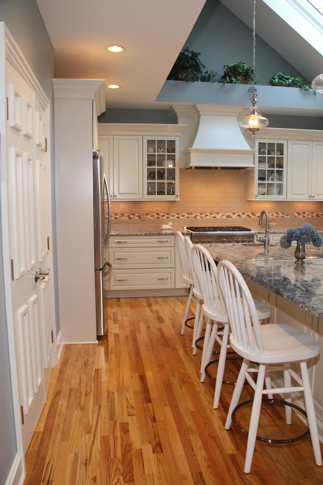 Klassisk inredning av ett stort flerfärgad flerfärgat kök, med en undermonterad diskho, luckor med upphöjd panel, vita skåp, granitbänkskiva, beige stänkskydd, stänkskydd i keramik, rostfria vitvaror, mellanmörkt trägolv, en köksö och brunt golv