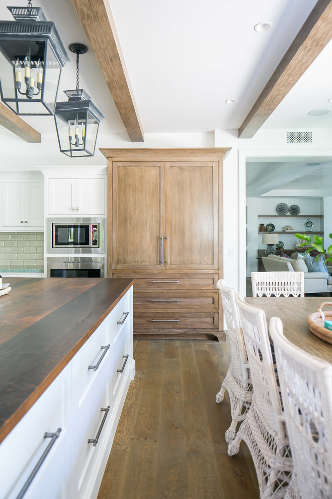 Example of a large island style u-shaped medium tone wood floor and brown floor eat-in kitchen design in Orange County with a double-bowl sink, shaker cabinets, white cabinets, wood countertops, white backsplash, subway tile backsplash, stainless steel appliances, an island and brown countertops