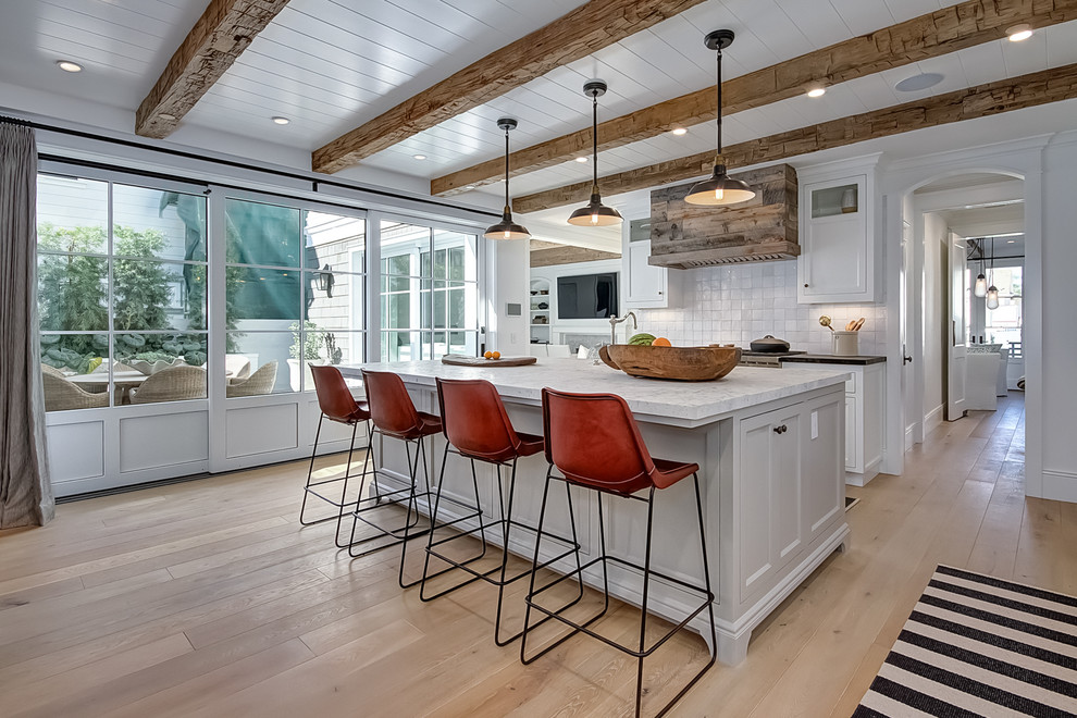 Photo of a coastal kitchen in Orange County with white cabinets, white splashback, light hardwood flooring, an island and shaker cabinets.