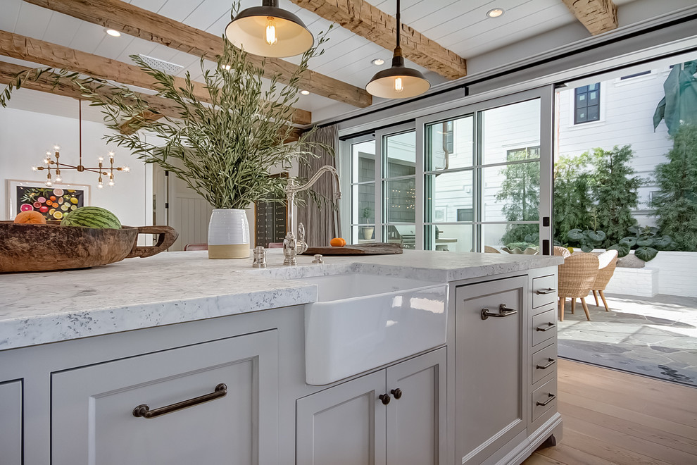 Zweizeilige Maritime Wohnküche mit Landhausspüle, Schrankfronten mit vertiefter Füllung, weißen Schränken, Küchenrückwand in Weiß, hellem Holzboden und Kücheninsel in Orange County