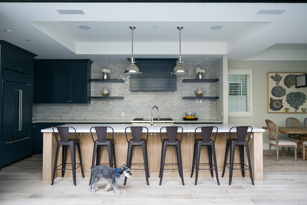 Klassische Wohnküche in L-Form mit Schrankfronten im Shaker-Stil, blauen Schränken, Küchenrückwand in Grau, Rückwand aus Metrofliesen, Elektrogeräten mit Frontblende, hellem Holzboden und Kücheninsel in Orange County