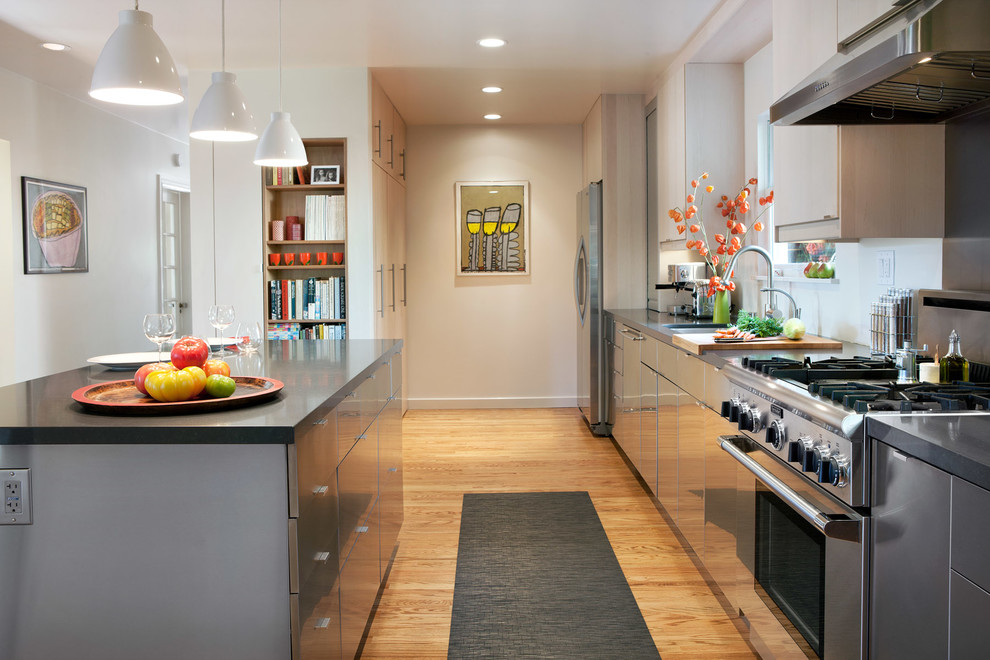 Example of a large trendy single-wall light wood floor and brown floor enclosed kitchen design in San Francisco with an undermount sink, flat-panel cabinets, stainless steel cabinets, limestone countertops, metallic backsplash, metal backsplash, stainless steel appliances and an island