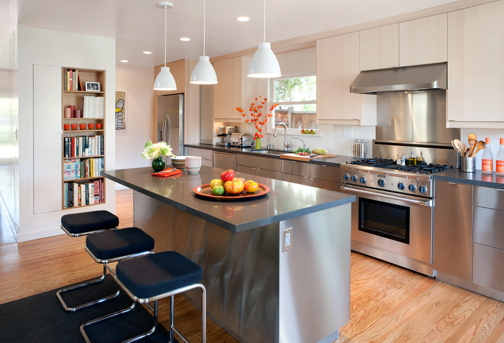 This is an example of a large contemporary single-wall enclosed kitchen in San Francisco with a submerged sink, flat-panel cabinets, stainless steel cabinets, stainless steel appliances, light hardwood flooring, an island, limestone worktops, metallic splashback, metal splashback and brown floors.