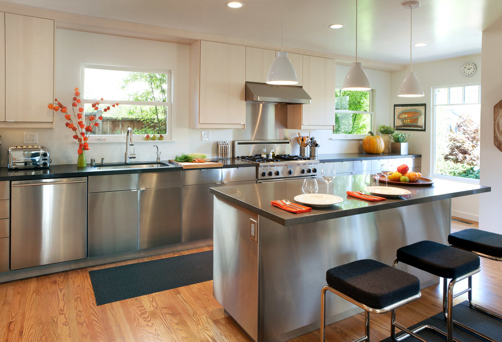 Exempel på ett avskilt, stort modernt linjärt kök, med en undermonterad diskho, släta luckor, skåp i rostfritt stål, bänkskiva i kalksten, stänkskydd med metallisk yta, stänkskydd i metallkakel, rostfria vitvaror, ljust trägolv, en köksö och brunt golv