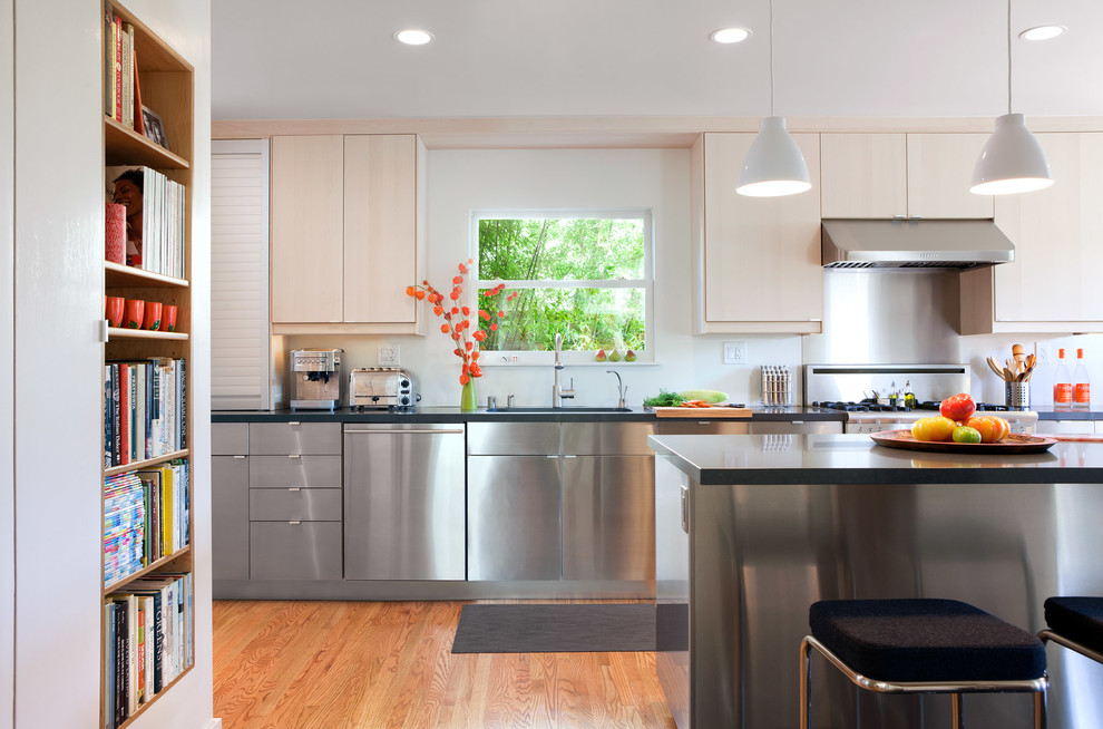 Example of a large trendy single-wall light wood floor and brown floor enclosed kitchen design in San Francisco with an undermount sink, flat-panel cabinets, stainless steel cabinets, limestone countertops, metallic backsplash, metal backsplash, stainless steel appliances and an island