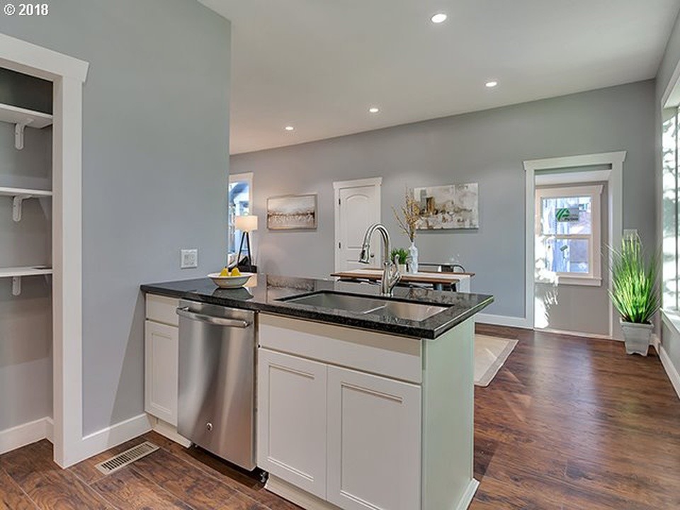 Exempel på ett litet amerikanskt grå grått kök, med en dubbel diskho, luckor med infälld panel, vita skåp, granitbänkskiva, grått stänkskydd, stänkskydd i tunnelbanekakel, rostfria vitvaror, mellanmörkt trägolv, en halv köksö och brunt golv