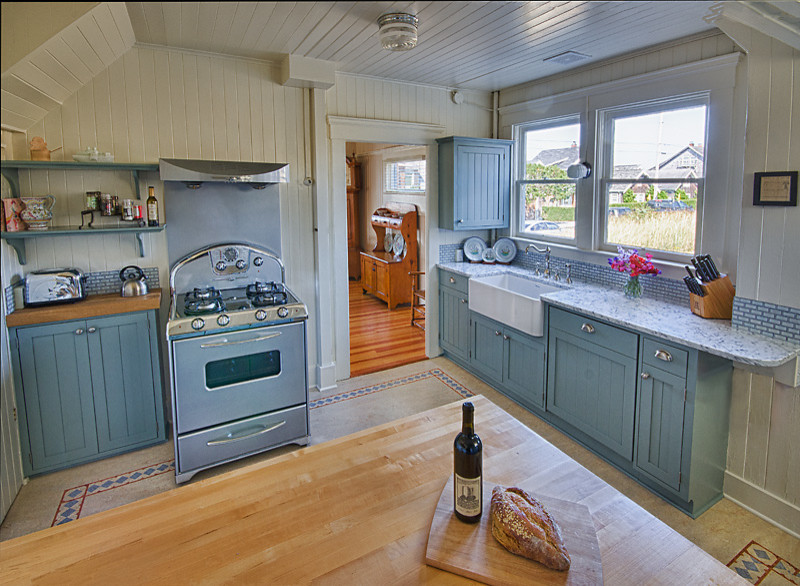 Photo of a medium sized coastal enclosed kitchen in Portland with a belfast sink, shaker cabinets, blue cabinets, wood worktops, stainless steel appliances, lino flooring and an island.