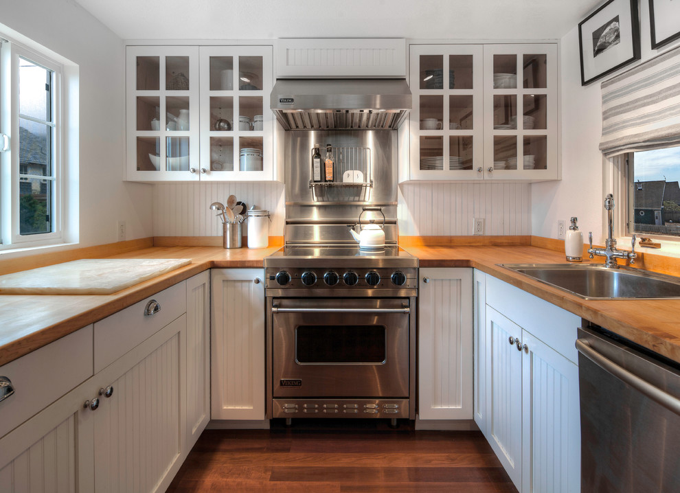 Nautical u-shaped enclosed kitchen in Seattle with a built-in sink, white cabinets, stainless steel appliances, white splashback, wood worktops and medium hardwood flooring.