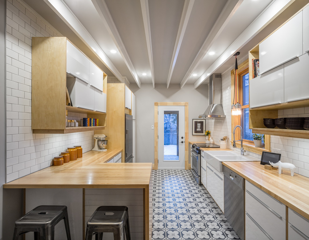 Design ideas for a small contemporary enclosed kitchen in Ottawa with a belfast sink, flat-panel cabinets, white cabinets, wood worktops, white splashback, metro tiled splashback, stainless steel appliances, ceramic flooring and a breakfast bar.