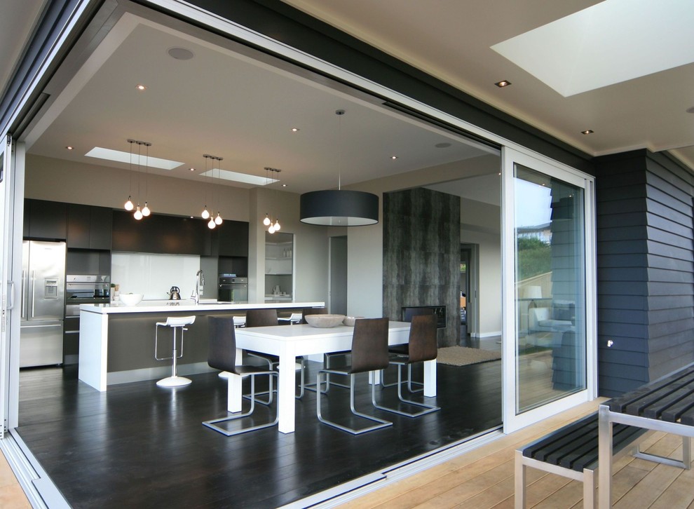Bild på ett stort funkis kök, med bruna skåp, bänkskiva i kvarts, vitt stänkskydd, stänkskydd i glaskakel, rostfria vitvaror, mörkt trägolv, en köksö och grönt golv