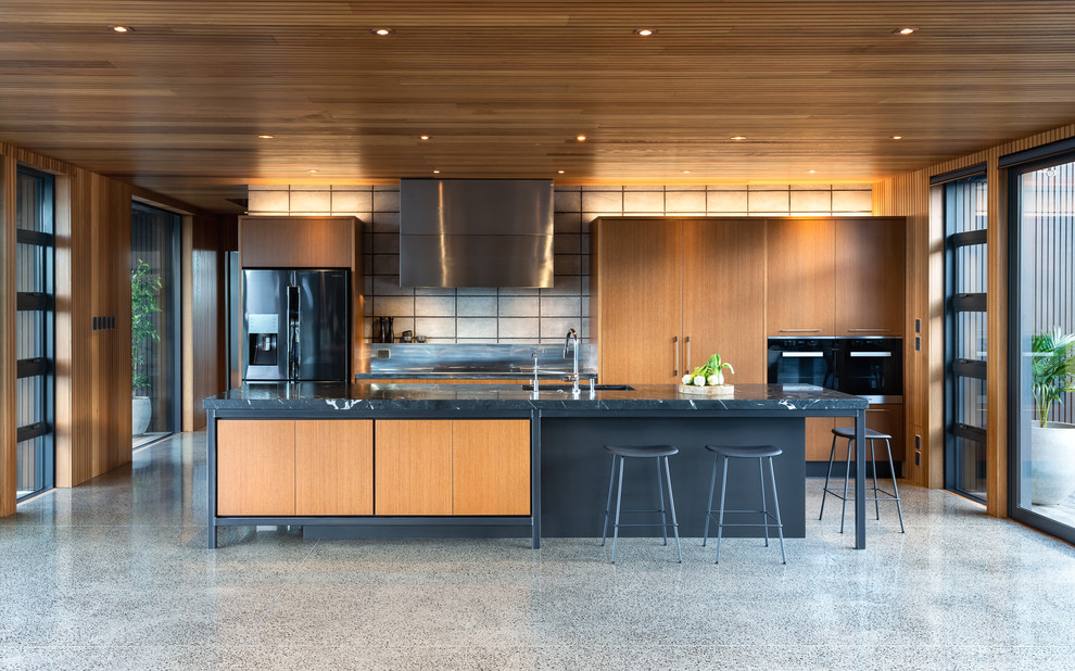 Einzeilige Moderne Wohnküche mit Unterbauwaschbecken, flächenbündigen Schrankfronten, grauen Schränken, Küchenrückwand in Beige, schwarzen Elektrogeräten, Kücheninsel, grauem Boden und schwarzer Arbeitsplatte in Auckland