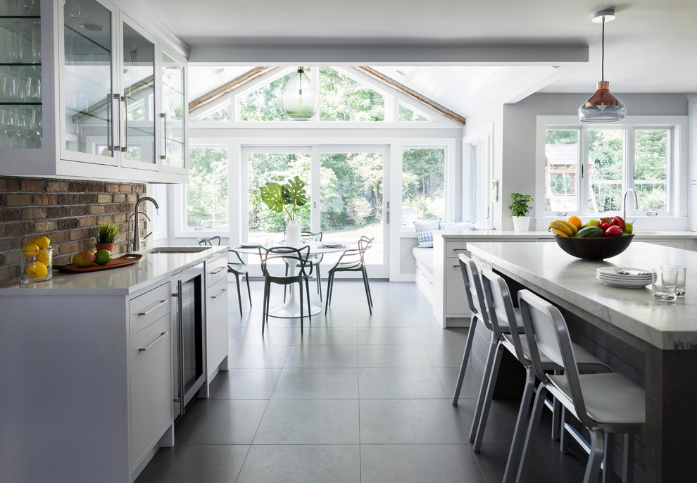 Inspiration for a mid-sized transitional l-shaped porcelain tile and gray floor eat-in kitchen remodel in New York with a single-bowl sink, flat-panel cabinets, white cabinets, quartzite countertops, brown backsplash, brick backsplash, stainless steel appliances and an island