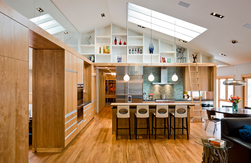 Идея дизайна: кухня-гостиная в стиле модернизм с техникой из нержавеющей стали, зеленым фартуком, фартуком из удлиненной плитки, плоскими фасадами, светлыми деревянными фасадами и барной стойкой