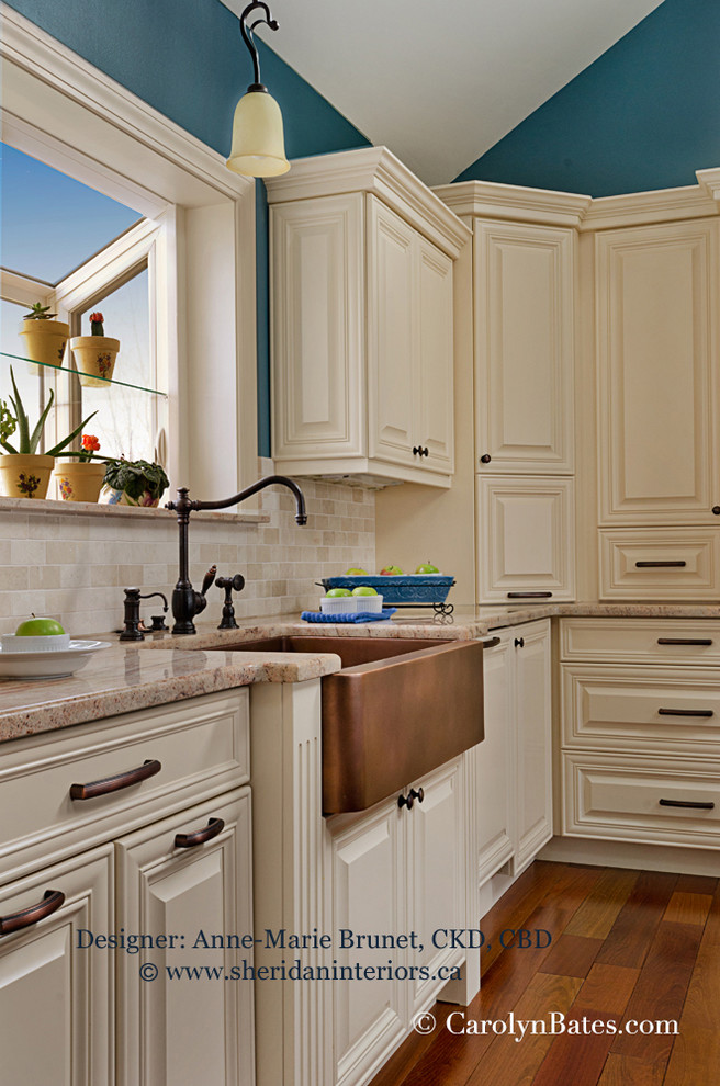 Klassisk inredning av ett l-kök, med en rustik diskho, luckor med upphöjd panel, beige skåp, laminatbänkskiva, svart stänkskydd, stänkskydd i tunnelbanekakel, rostfria vitvaror och mellanmörkt trägolv