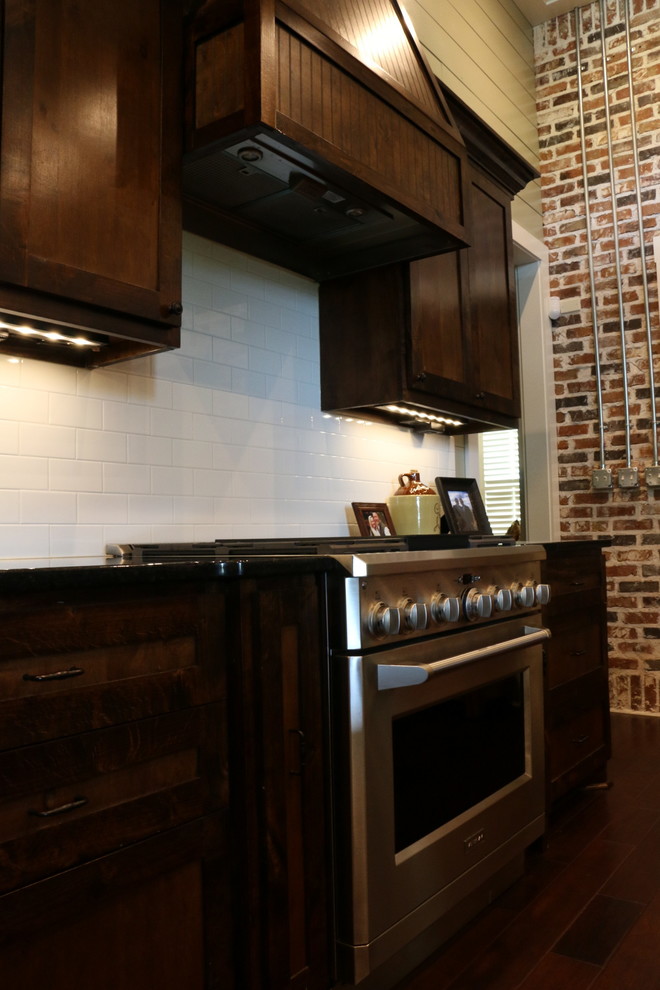 Bild på ett stort industriellt kök, med skåp i shakerstil, skåp i mörkt trä, granitbänkskiva, vitt stänkskydd, stänkskydd i tunnelbanekakel, rostfria vitvaror, mellanmörkt trägolv, en köksö och en dubbel diskho