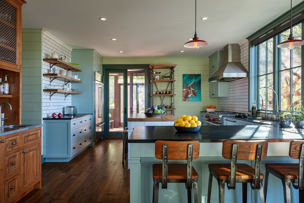 Farmhouse u-shaped medium tone wood floor and brown floor eat-in kitchen photo in San Francisco with an undermount sink, shaker cabinets, green cabinets, white backsplash, subway tile backsplash, stainless steel appliances, an island and black countertops