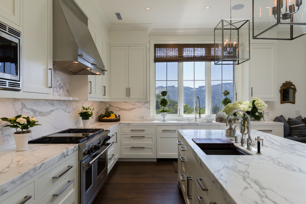 Exempel på ett klassiskt l-kök, med en undermonterad diskho, skåp i shakerstil, vita skåp, vitt stänkskydd, rostfria vitvaror, mörkt trägolv, en köksö och stänkskydd i marmor