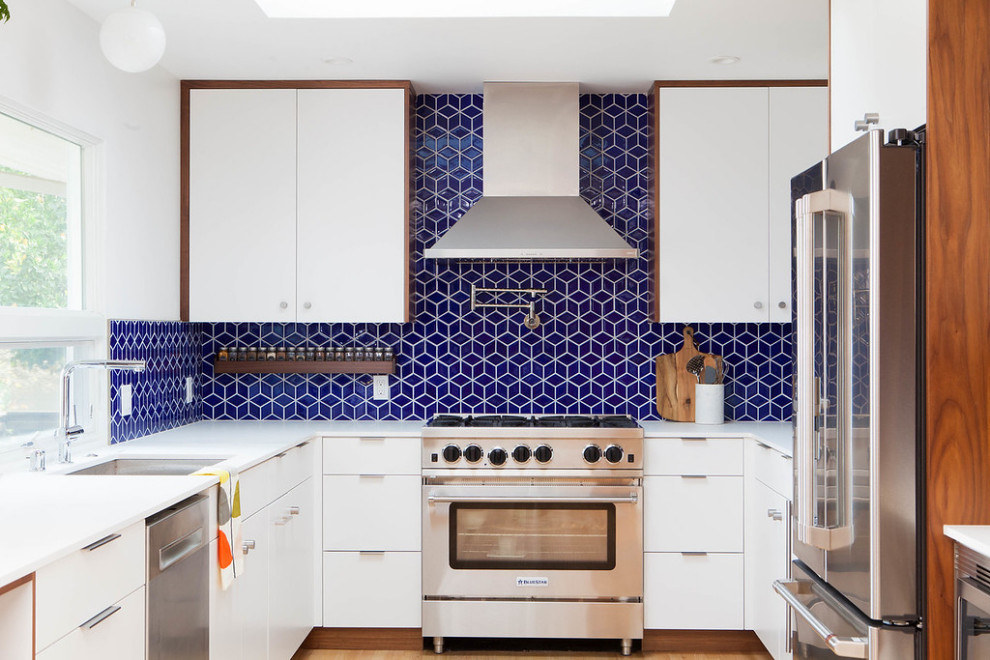 Mid-century modern light wood floor kitchen photo in San Francisco with an undermount sink, flat-panel cabinets, white cabinets, quartz countertops, blue backsplash, ceramic backsplash, stainless steel appliances, a peninsula and white countertops