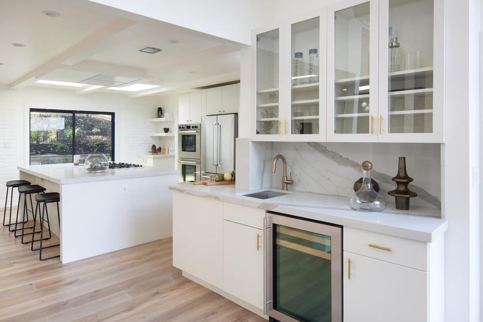 Design ideas for a large midcentury l-shaped open plan kitchen in San Francisco with a submerged sink, flat-panel cabinets, white cabinets, engineered stone countertops, white splashback, stainless steel appliances, light hardwood flooring, an island and white floors.