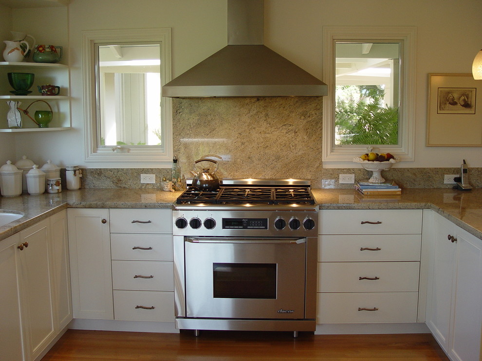 Klassisk inredning av ett kök, med rostfria vitvaror, granitbänkskiva, vita skåp, brunt stänkskydd och stänkskydd i sten