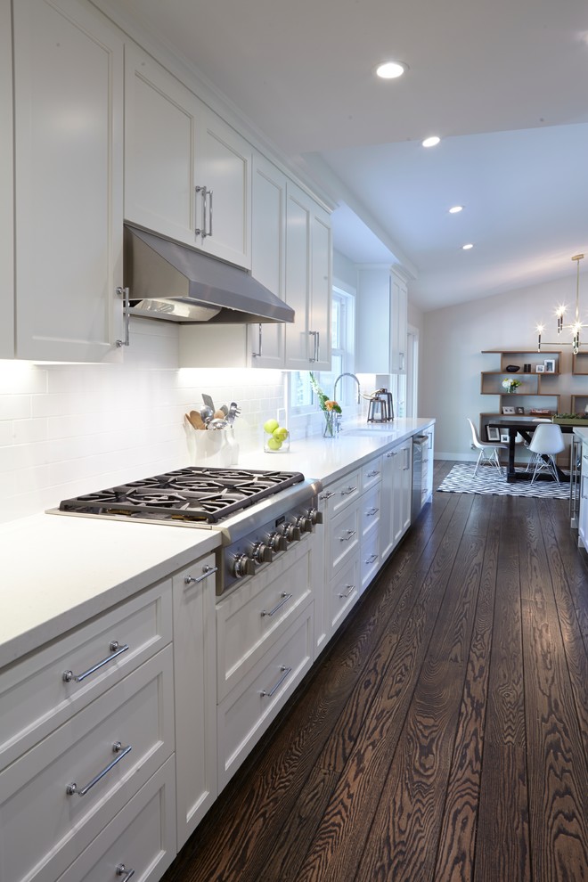Large midcentury galley kitchen/diner in San Francisco with a submerged sink, shaker cabinets, white cabinets, engineered stone countertops, white splashback, metro tiled splashback, stainless steel appliances, dark hardwood flooring and an island.