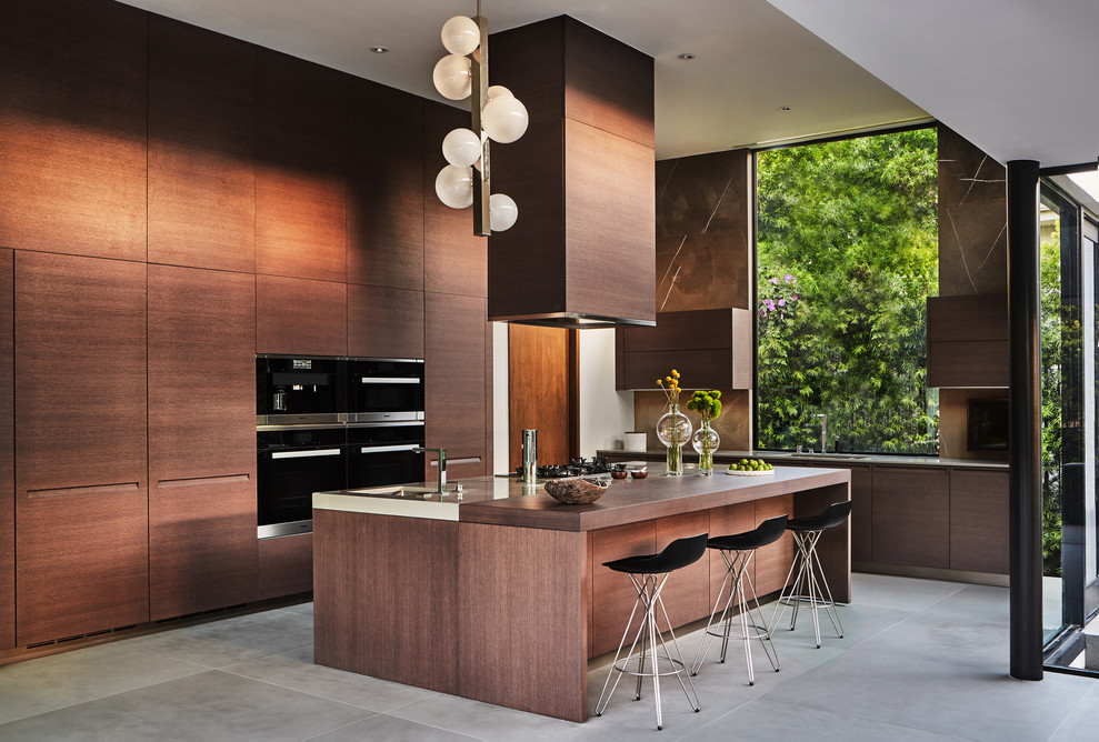 Moderne Küche in L-Form mit flächenbündigen Schrankfronten, dunklen Holzschränken, Küchengeräten aus Edelstahl, Kücheninsel, grauem Boden und grauer Arbeitsplatte in Los Angeles